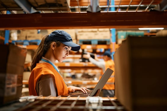 Supply chain outlook- female warehouse manager with laptop in distribution center.